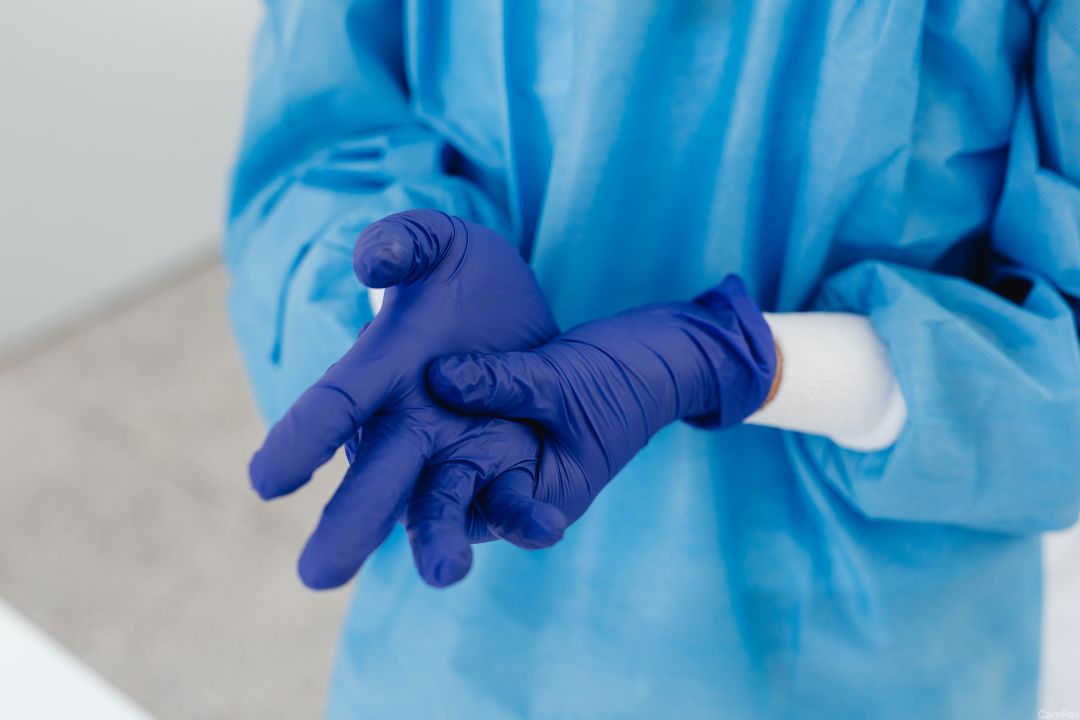 A nurse practices sterile technique by putting on sterile gloves and gown.