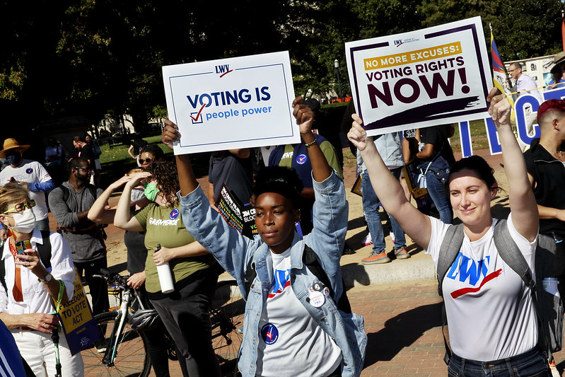 two young women holding up "voting is people power" signs at a rally