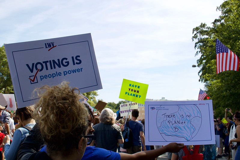 People holding signs at a peaceful protest to rally around environmental causes. The main signs say "voting is people power" and "there is no planet B"