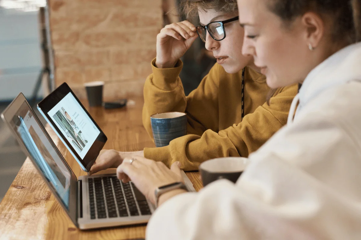 Two colleagues collaborating on laptops at a wooden table.