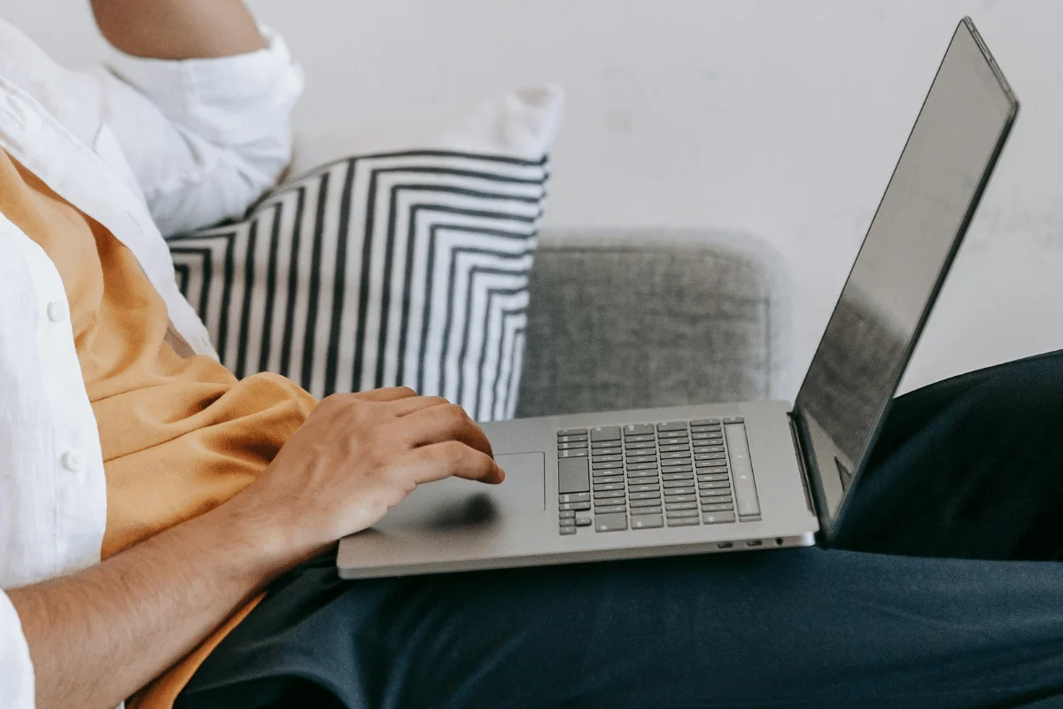 Person working on a laptop while sitting on a couch with a striped pillow.