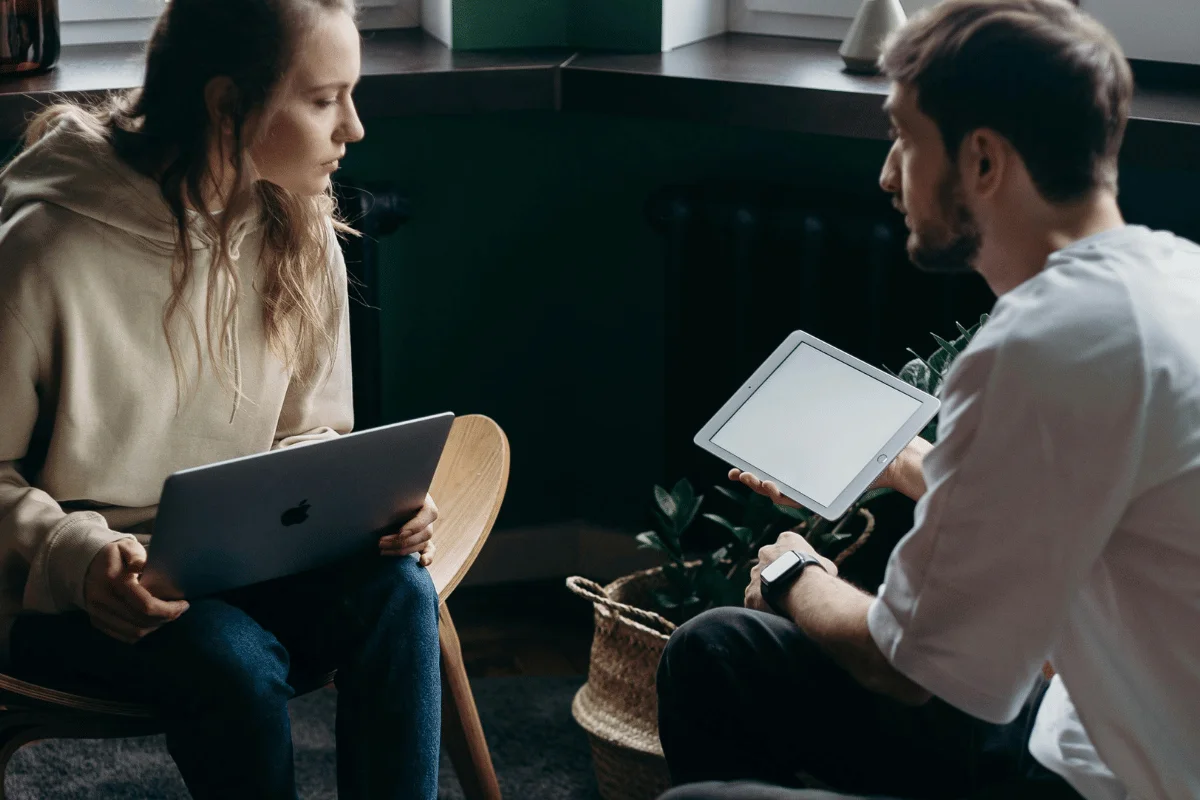 Focused pair in a serious discussion with a laptop and tablet in hand.