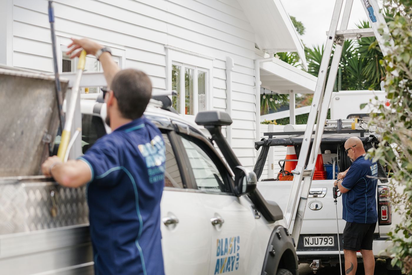 Two Blast Away Guys technicians loading equipment from their trucks before a house wash job in Northland.