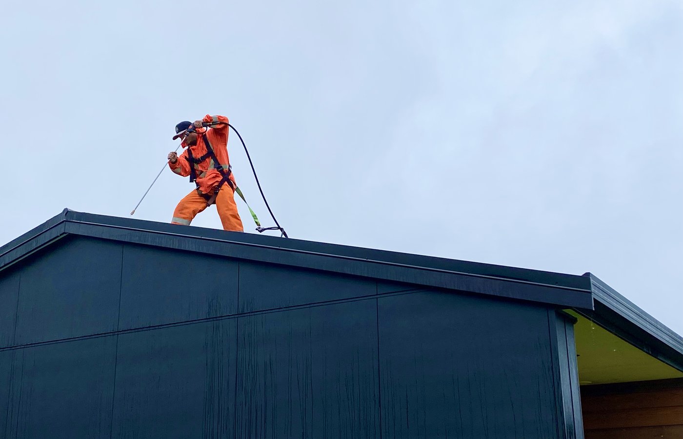 Blast Away Guys technician applying roof treatment on a black house roof in Whangarei.
