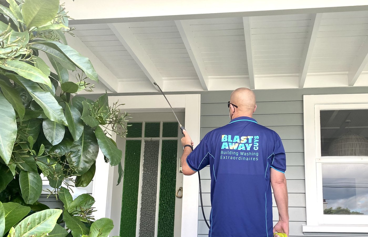Blast Away Guys technician applying bug and spider treatment to the eaves of a house.