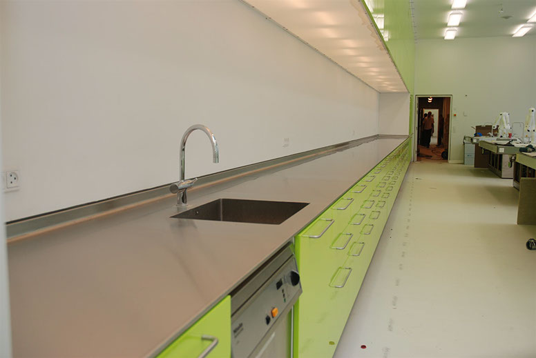 Long stainless worktop with integrated sink above green cabinets