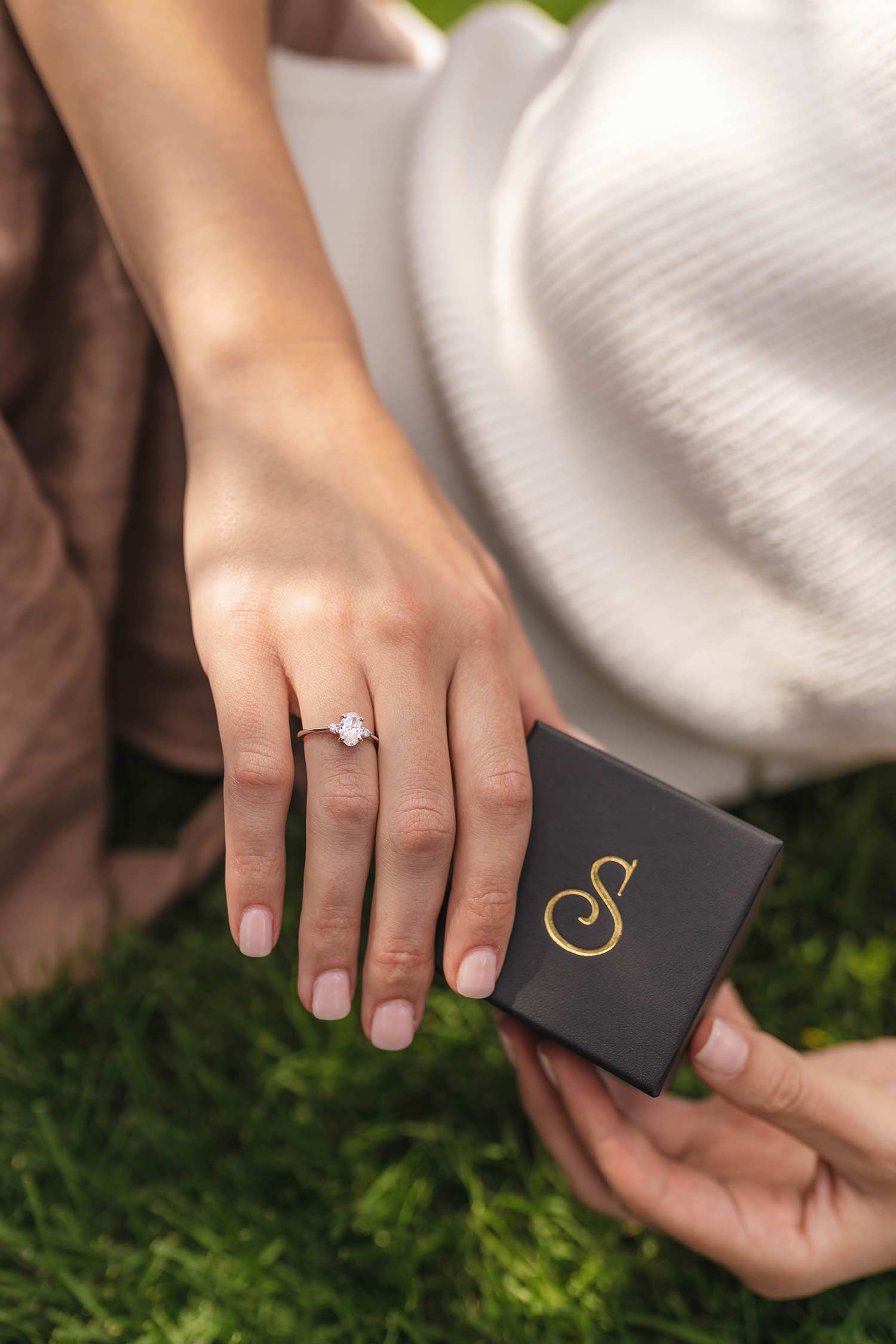 a closeup of a women's hand with a n engagement ring while holding a Swanson's Jewellers ring box