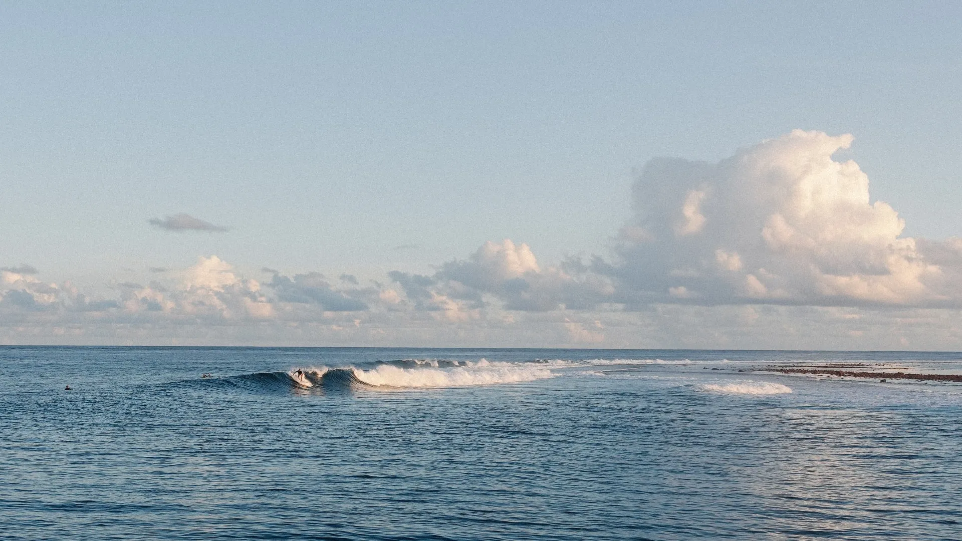Surfer riding a small wave on a calm ocean under a partly cloudy sky during daylight.