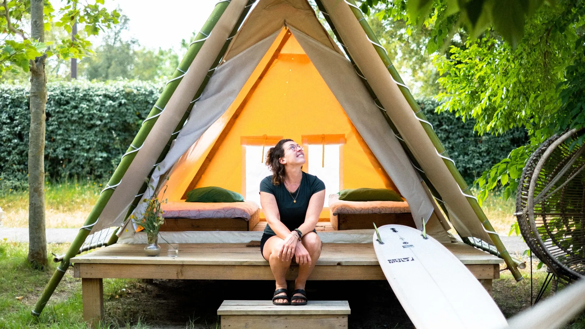 girl with her surfboard in front of tipi tent
