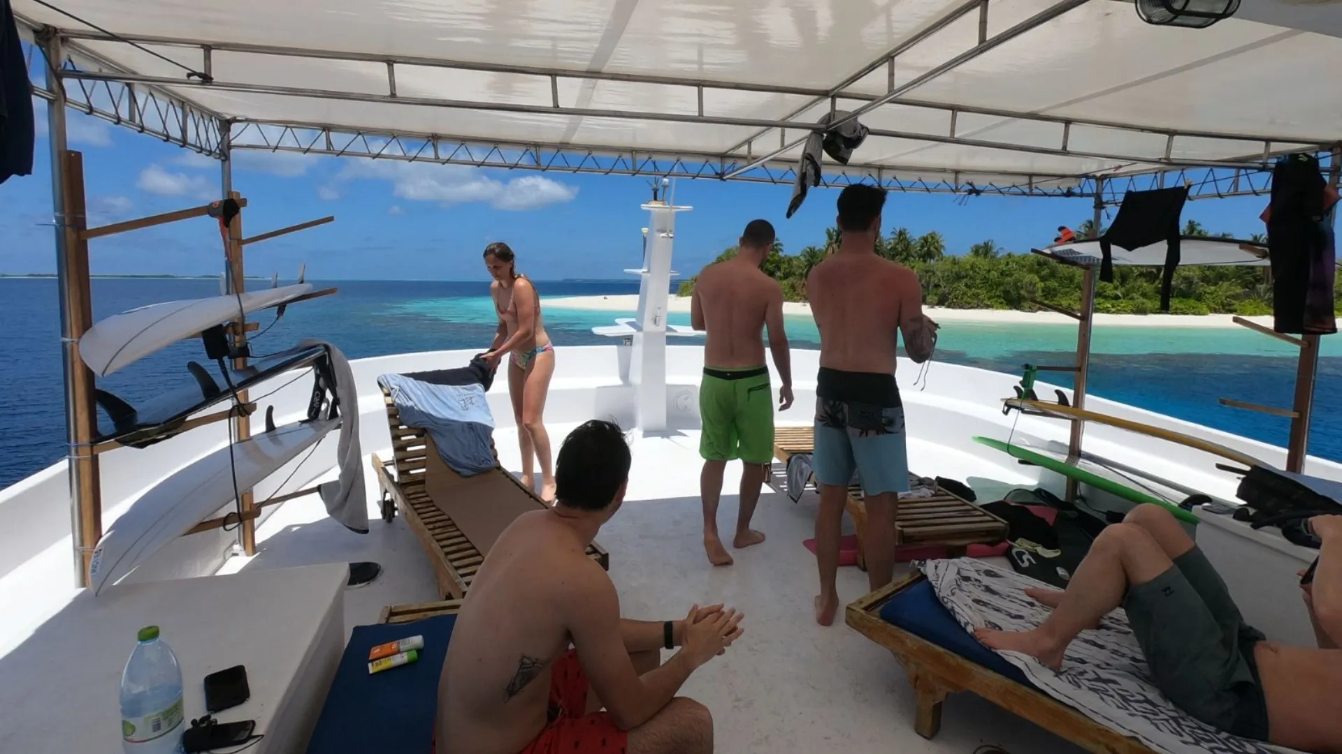 people and surfboards on top of a boat in front of a deserted island