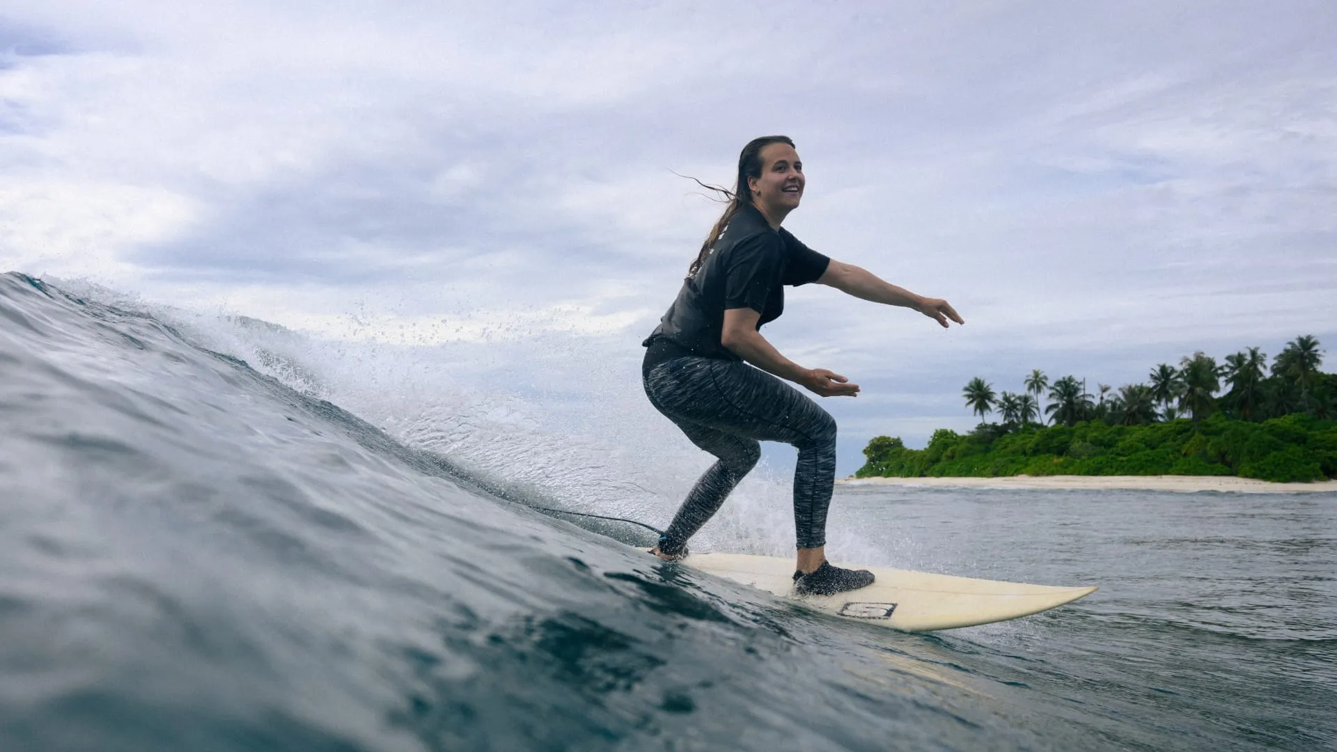 Smiling surfer girl bottom turning backside on a clean wave, shot from the water