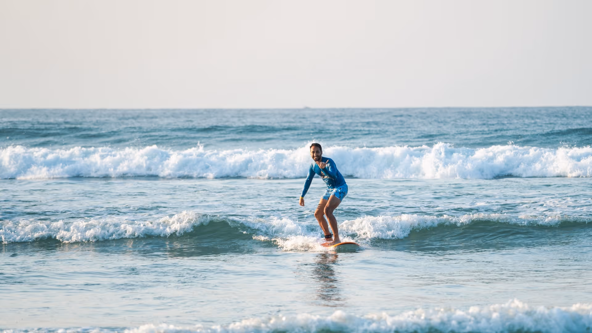 beginner riding a wave and throwing a shaka