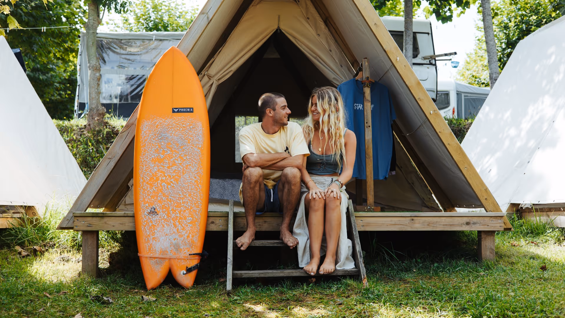 couple and surfboard in front of the tent