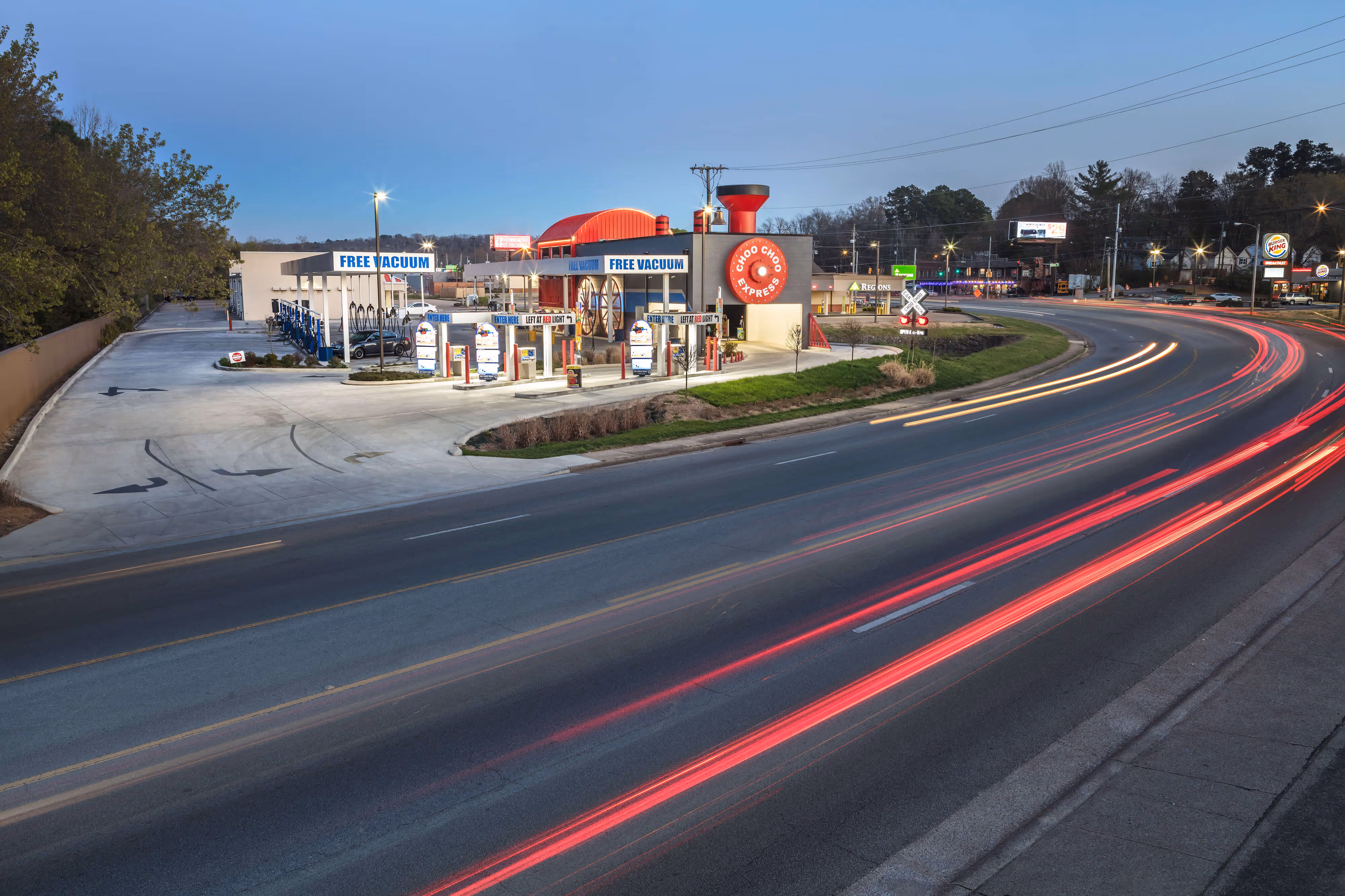 Choo Choo Express car wash station at dusk with light trails from passing cars on a curved road.