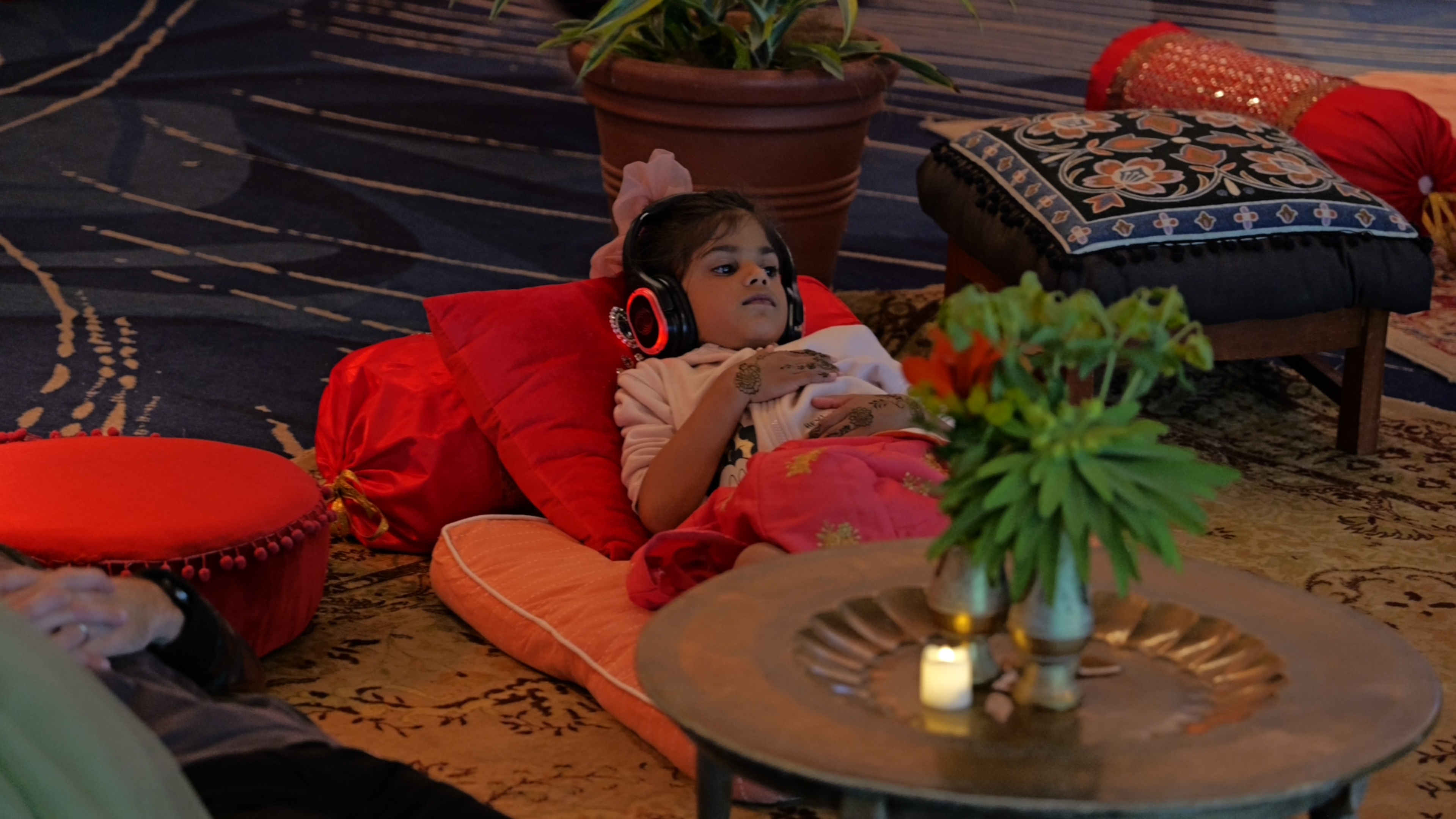 A young guest lying back on cushions wearing silent-disco headphones, henna on her hands