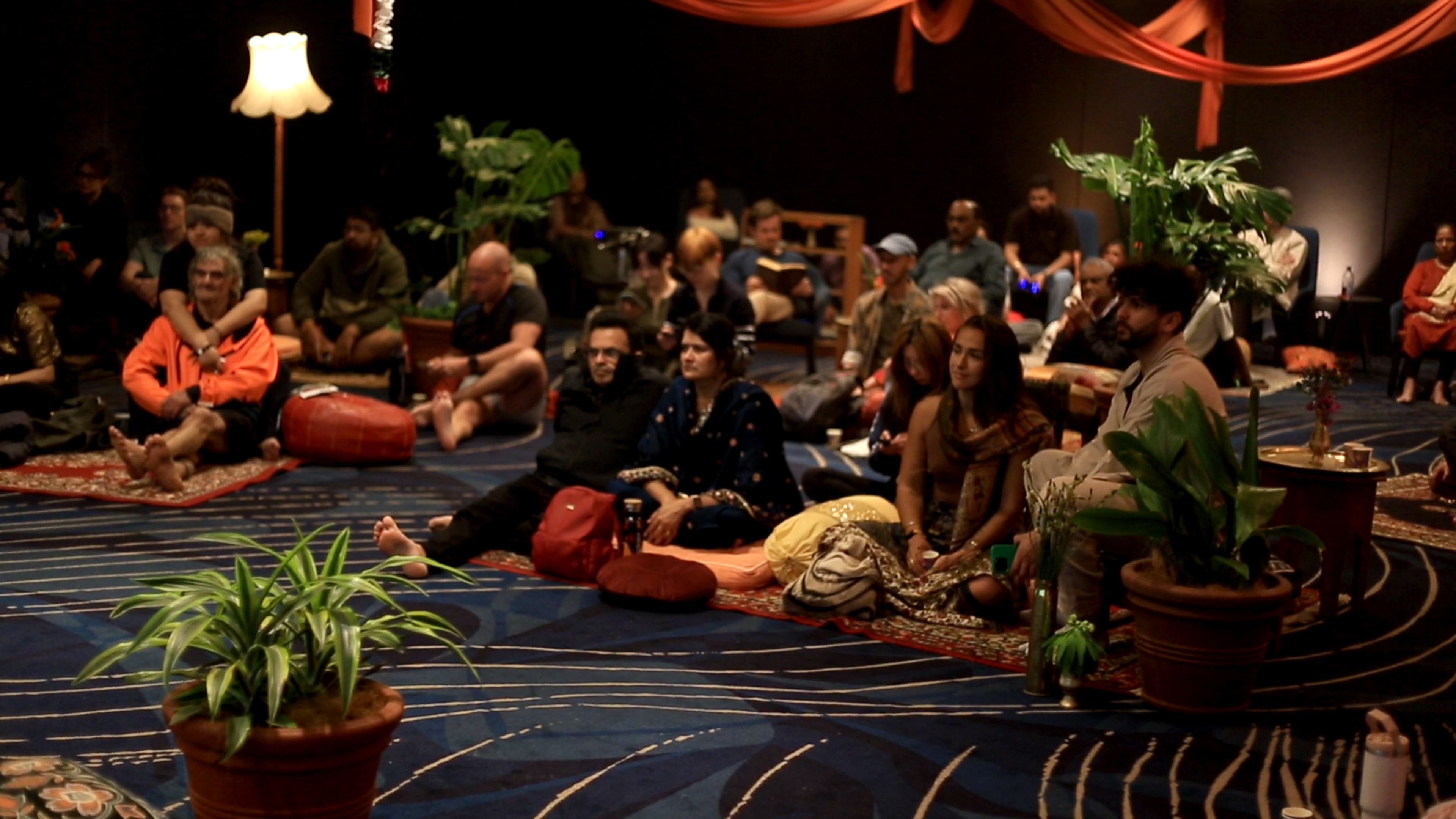 Festival-goers seated on cushions and rugs, listening to the live performance