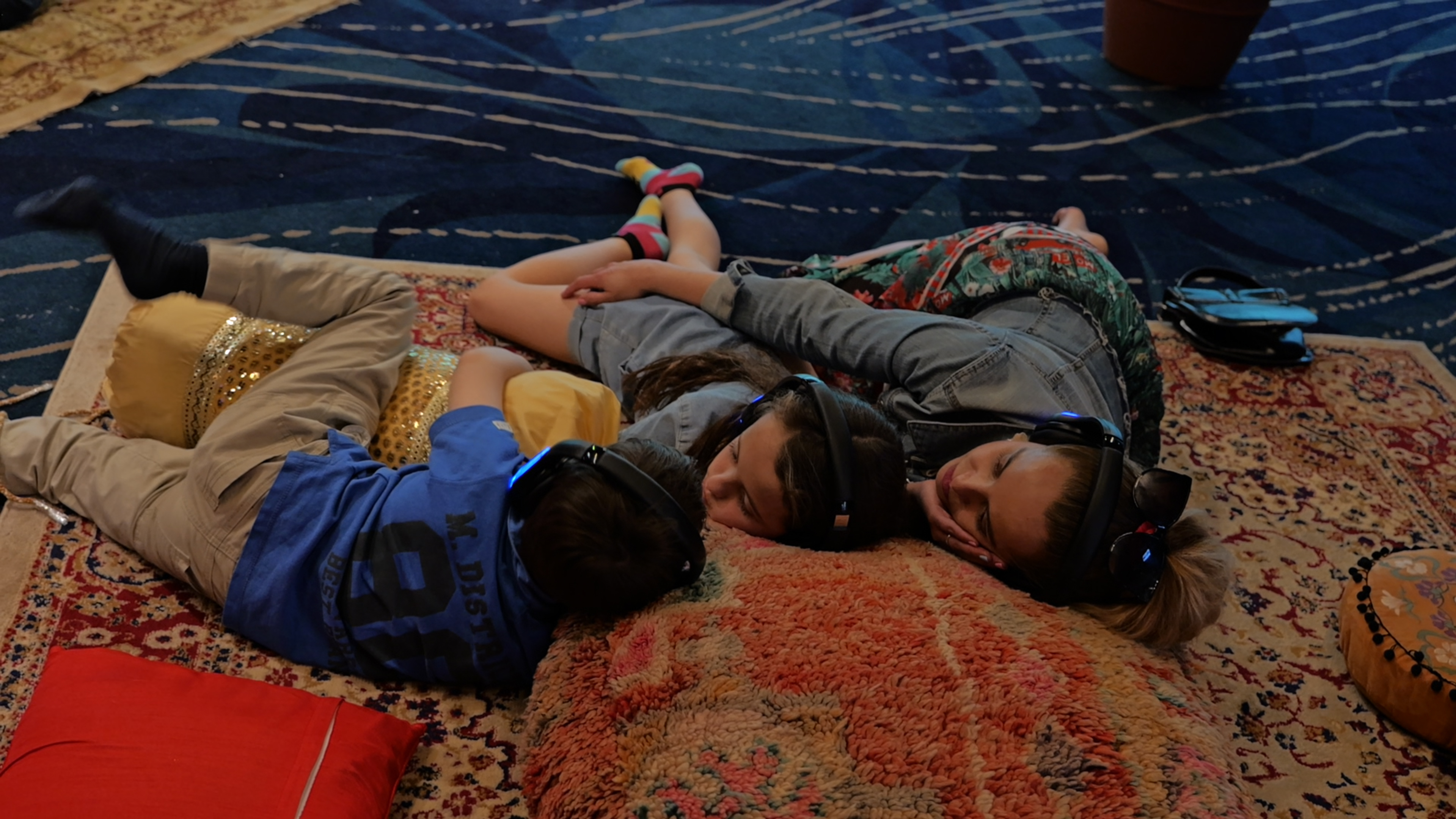 Three children lying on rugs together, all wearing silent-disco headphones