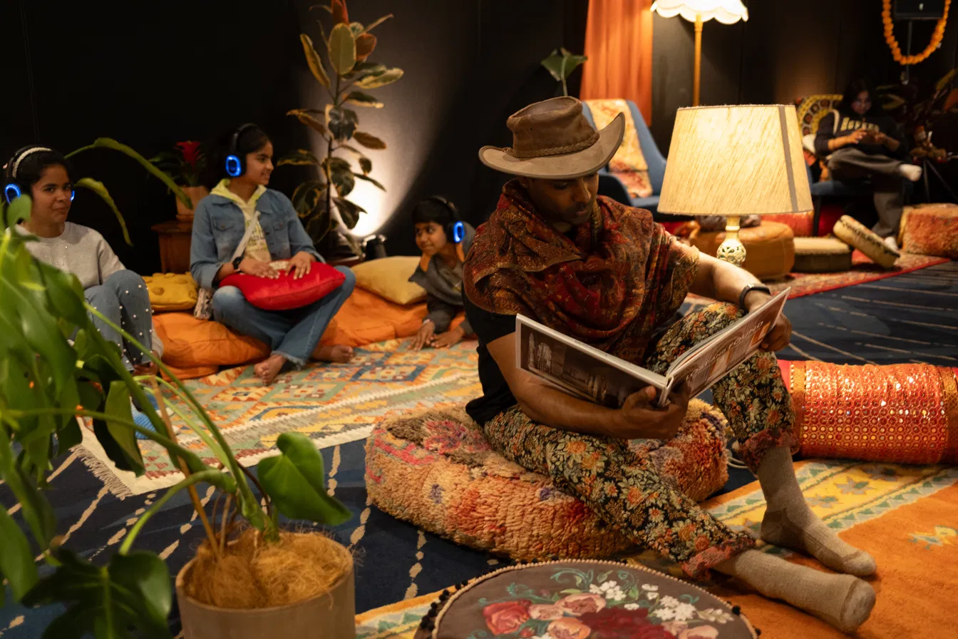 A guest wrapped in a patterned shawl reading a book on a cushion, surrounded by other guests relaxing nearby