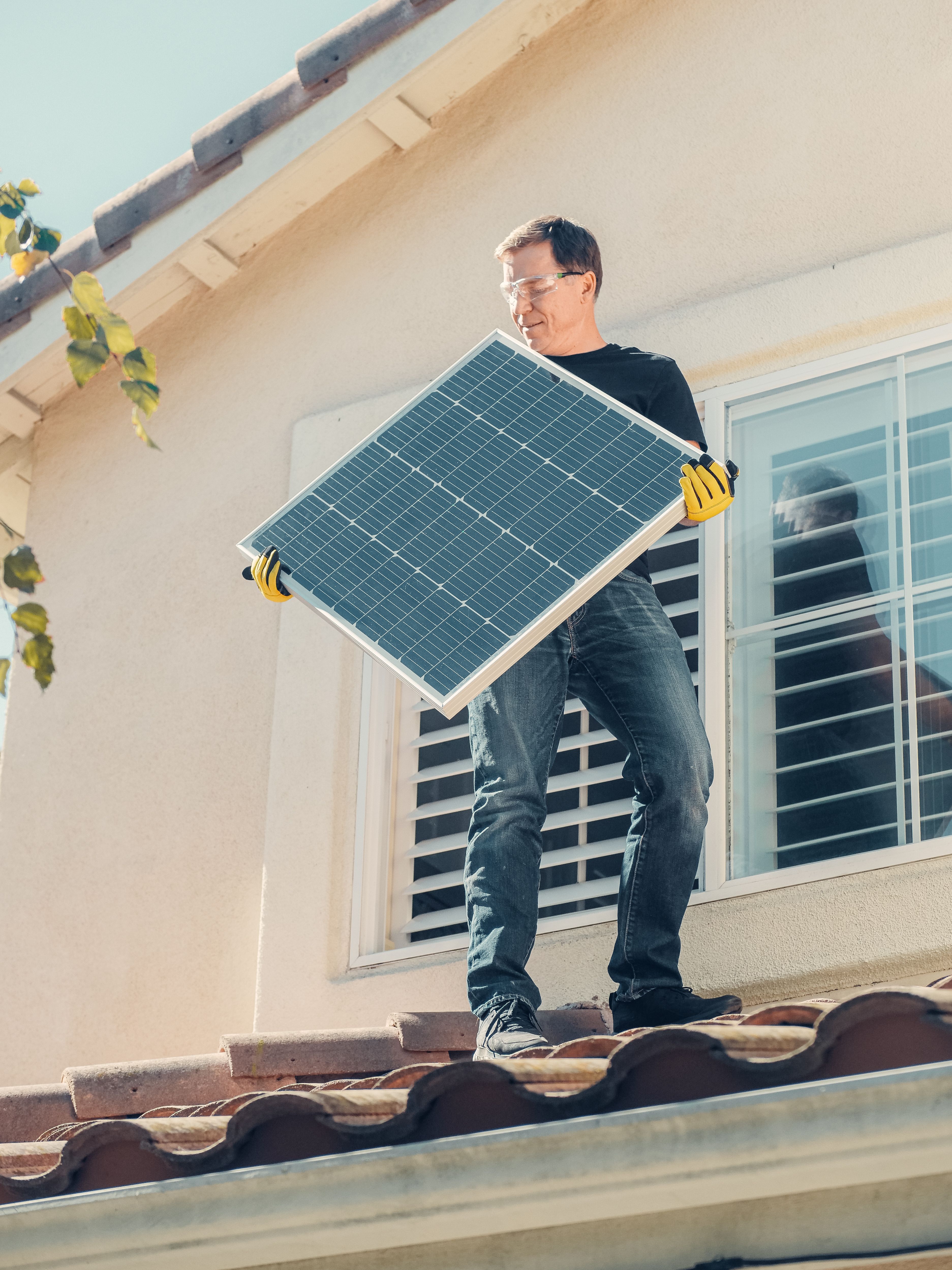 Solar installer carrying a solar panel across a homeowner's tile roof