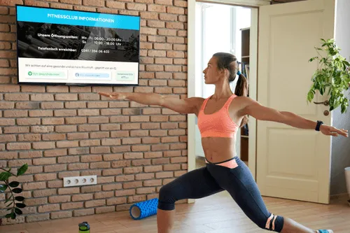 Woman in sportswear doing exercises in front of a screen on which the air quality parameters are displayed by the air-Q Smart Widgets