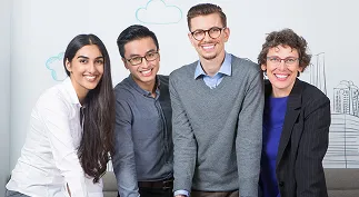 Four diverse colleagues smiling together in a casual office setting with drawn clouds and buildings on the wall behind them.