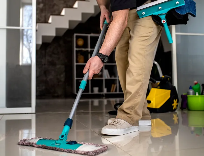 Person mopping a shiny tiled floor using a blue mop with a cleaning caddy attached to their waist.