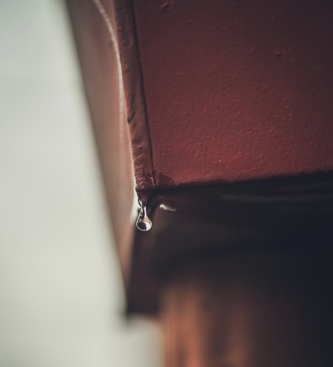 Close-up of a brown rain gutter with a water droplet at the edge, highlighting the importance of proper drainage and home maintenance for spring upkeep.
