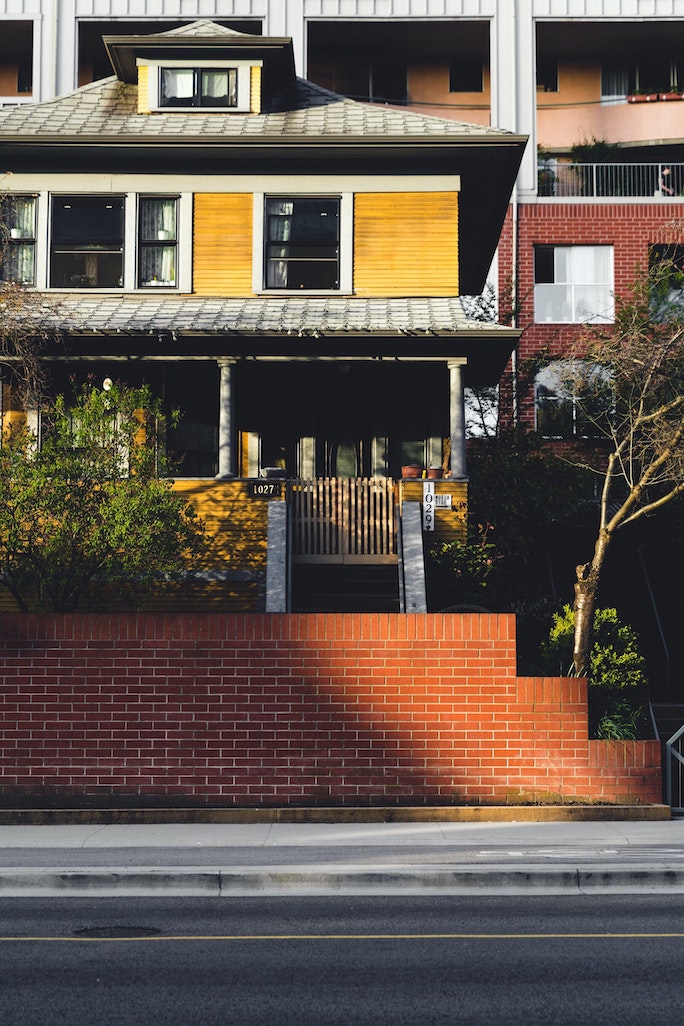 Modern yellow house with a red brick retaining wall and landscaped greenery, showcasing strong curb appeal and exterior design for home staging inspiration.