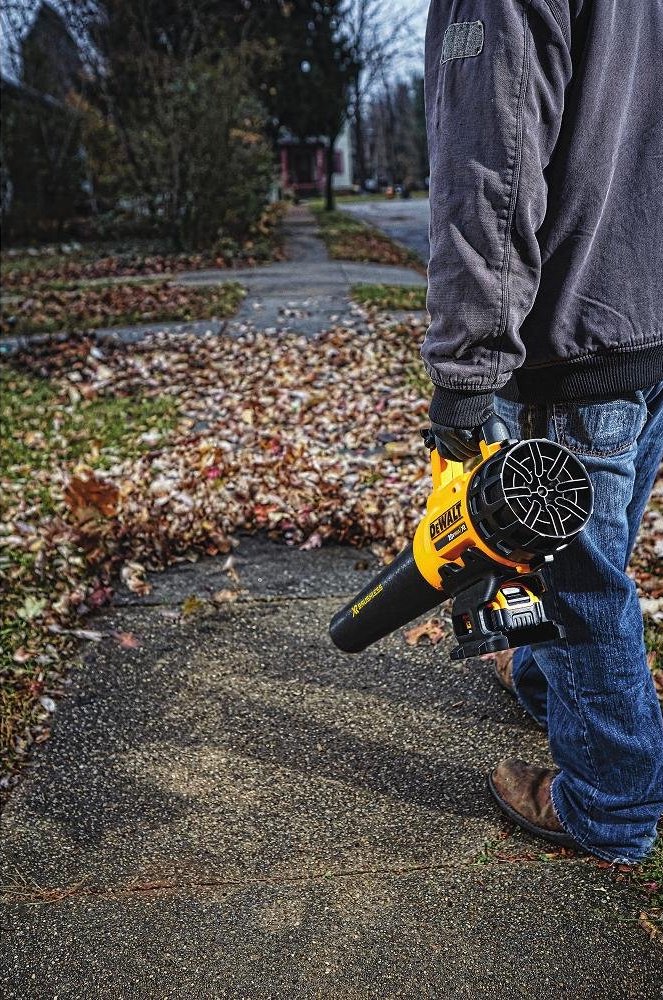 A person using a yellow leaf blower to clear fallen autumn leaves from a sidewalk, demonstrating efficient yard cleanup and seasonal landscape maintenance.