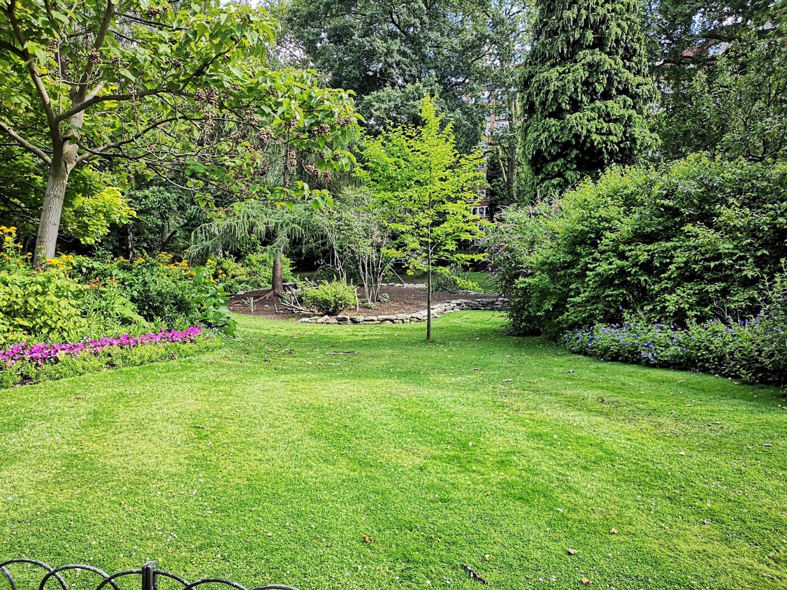 Beautiful landscaped garden with lush green grass, colorful flower beds, and trees, showcasing a well-maintained backyard design for outdoor inspiration.