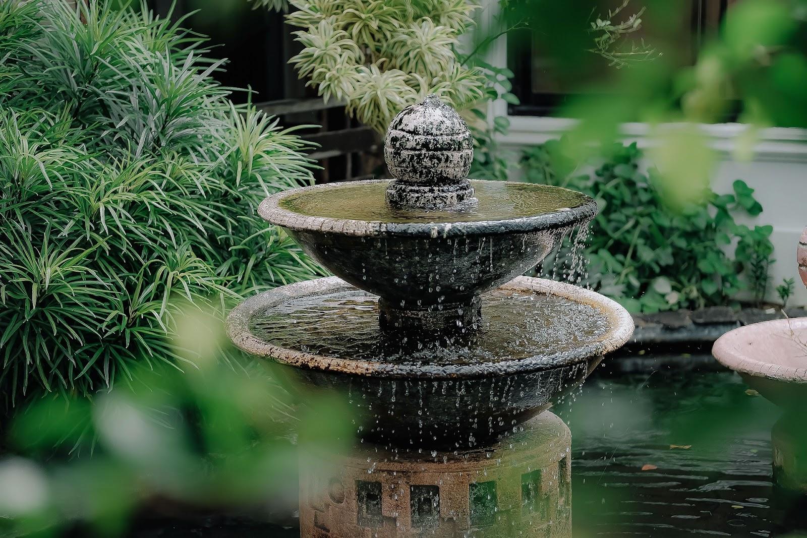 Elegant tiered stone fountain with cascading water surrounded by lush green plants, creating a tranquil and refreshing focal point in a garden setting.