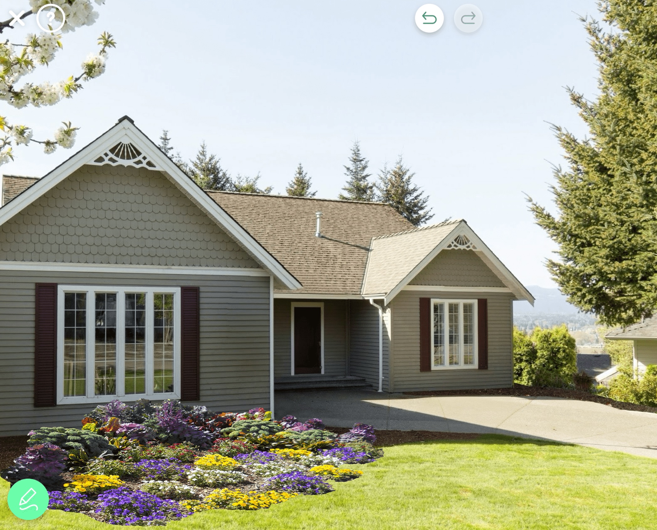 A light-gray suburban home with white trim and a newly visualized front-yard flower bed featuring colorful seasonal plants designed using iScape.