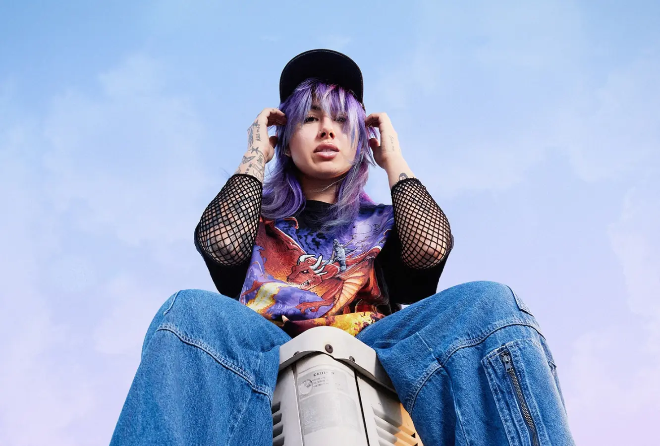 A young woman sitting on a box looking down as she holds her hands next to her head.