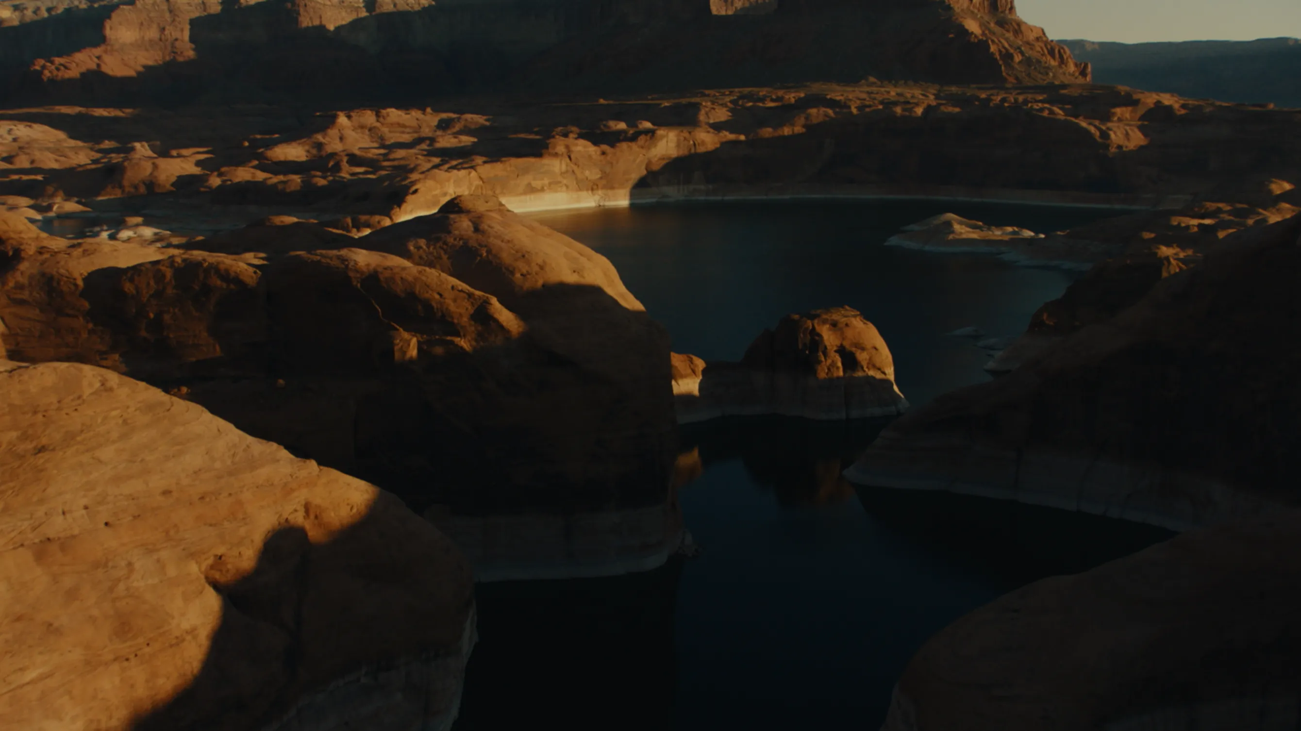 Sunlit rocky canyon with dark waters in shadows, showcasing layered rock formations and cliffs at dusk.