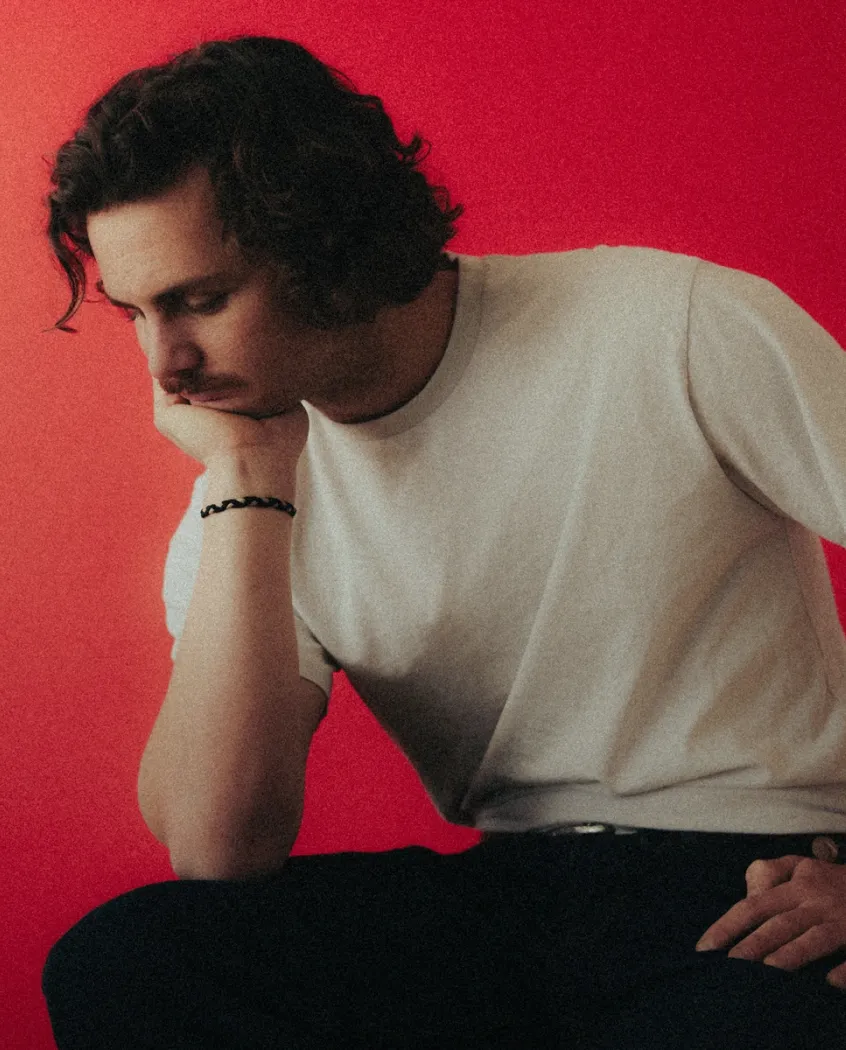 Young woman wearing a knitted hat with a pom-pom and a blue jacket, outdoors near rocky terrain at dusk.