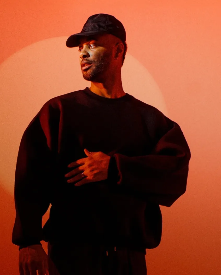 Young woman wearing a knitted hat with a pom-pom and a blue jacket, outdoors near rocky terrain at dusk.