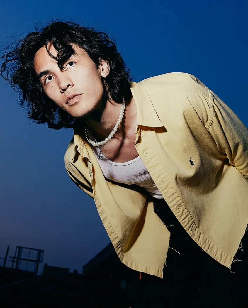Young woman wearing a knitted hat with a pom-pom and a blue jacket, outdoors near rocky terrain at dusk.