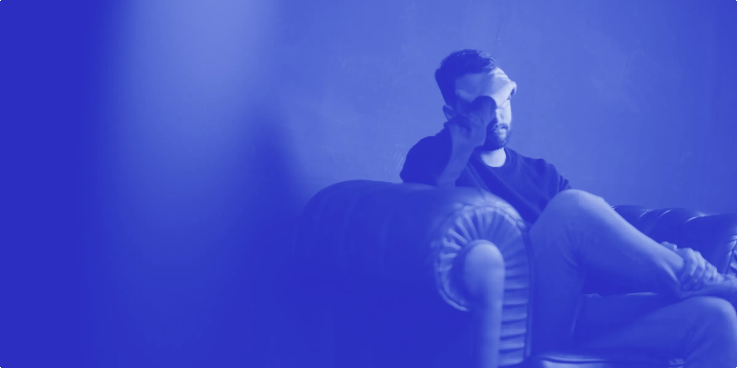 A man sitting on a couch looking down with his hand on his head, styled with a blue gradient overlay