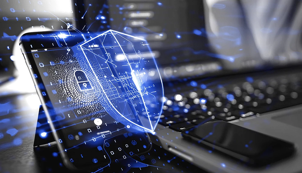 A person's hands on a notebook. One hand is on the keyboard writing and the other is holding a smartphone. 