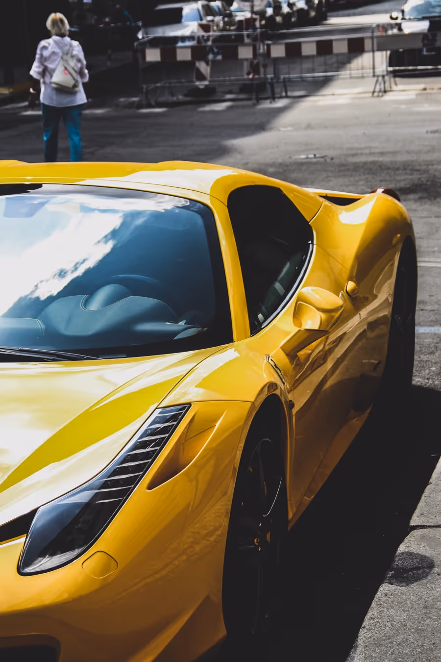 Close-up of a yellow sports car parked on the street with a person walking in the background.