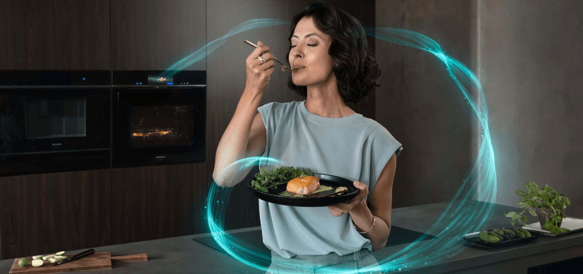 Frau probiert ein Gericht in einer modernen Siemens Küche mit smartem Backofen und KI-gestützter Kochtechnologie.
