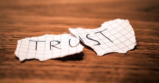 Photo of paper on which is written the word trust, torn in two pieces