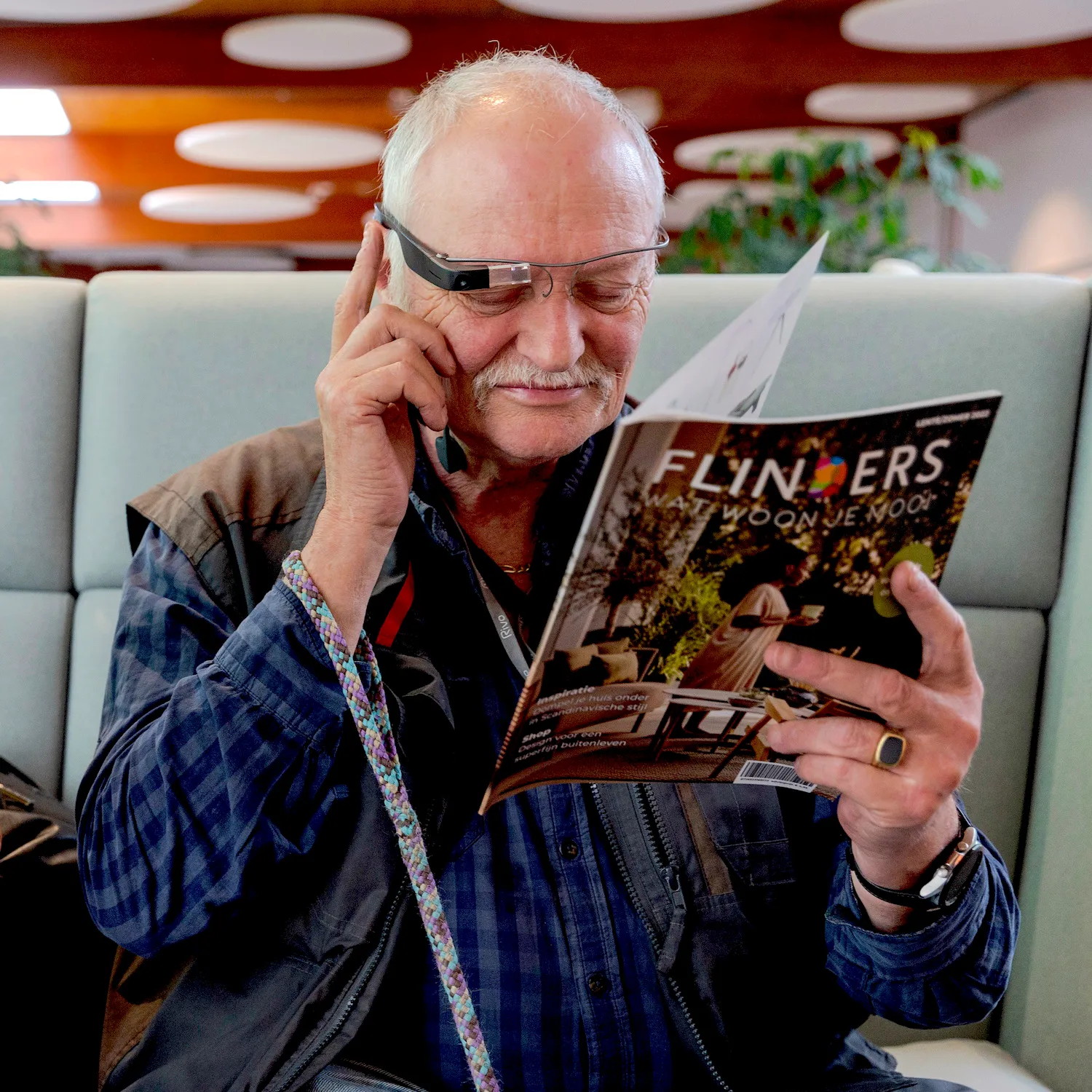 A Picture of an ederly man reading a magazine with his Envision Glasses