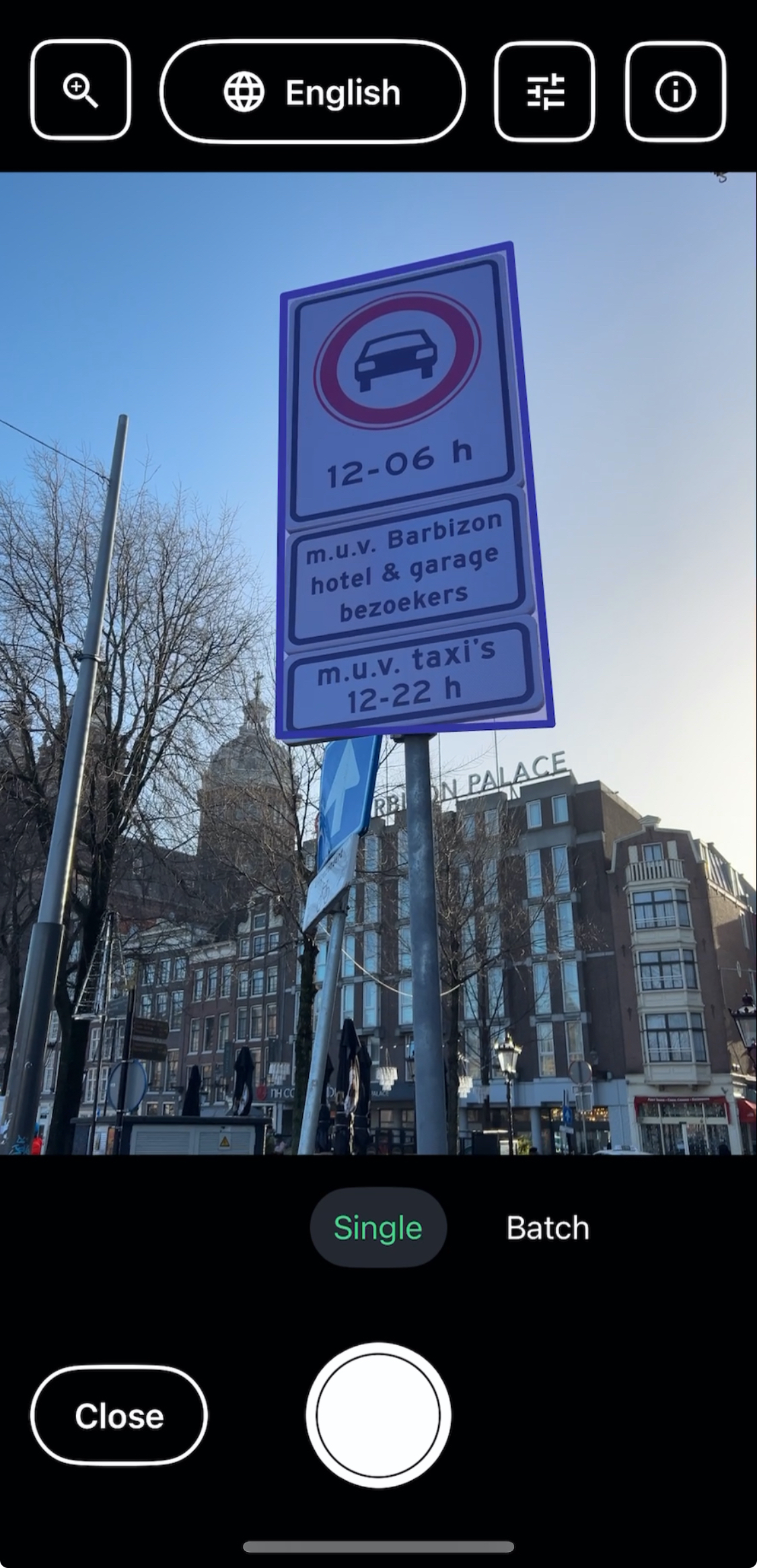 The image shows the Envision app interface with a street scene in the background. A parking sign is prominent in the upper part of the image, indicating restrictions with the symbol of a car and times listed in blue. Below, the text specifies exceptions for "Barbizon hotel & garage bezoekers" and "taxi's" with corresponding times. Traditional Dutch buildings, a clear sky, and bare trees form the backdrop. The app's control icons for language selection, scanning options, and navigation are visible at the top and bottom.