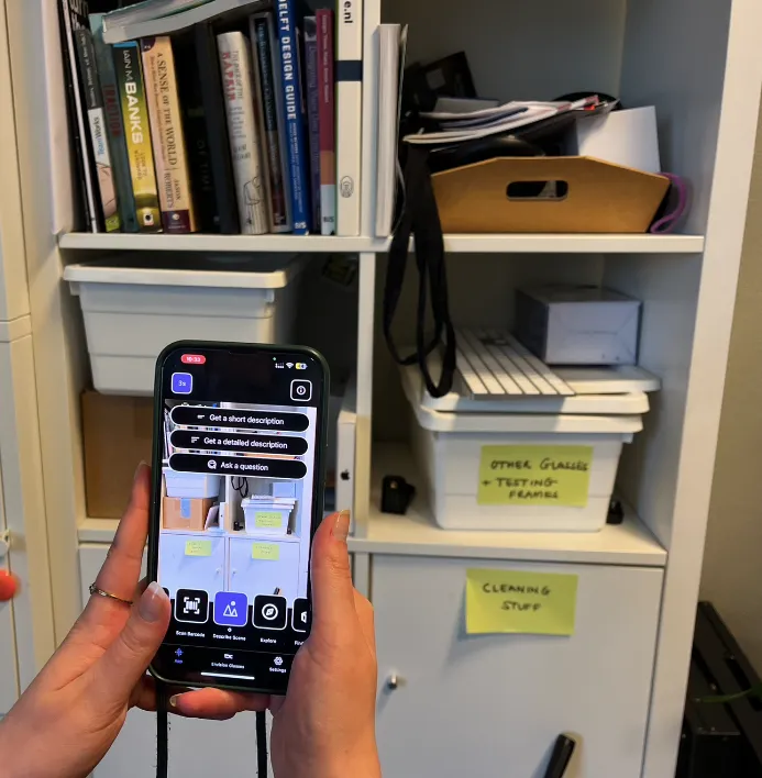 The Envision App is pointed at a shelf and the describe scene feature shows th epossibility o have short but concise description or long descriptions - as well as a 3-timer second at the botton top of the screen.