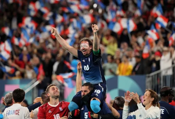 A photo of a French footballer in the blind football celebrating his team's winning. Where the French player Frederic Villeroux, sits on top of one of his team-mates