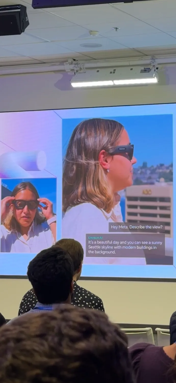 Alt: A presentation slide showcasing Meta's AI technology. It features images of a woman wearing smart glasses, with a text overlay showing an AI-generated description of the scene: "It's a beautiful day and you can see a sunny Seattle skyline with modern buildings in the background." The slide demonstrates AI-powered scene description capabilities.