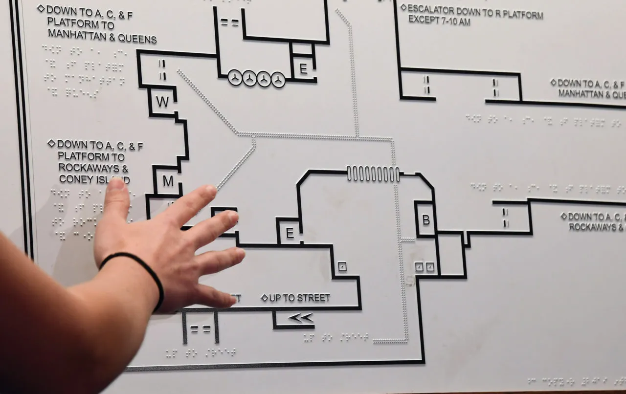 A hand exploring an accessible subway map designed with tactile pathways and braille text, providing navigation support for individuals who are blind or have low vision.