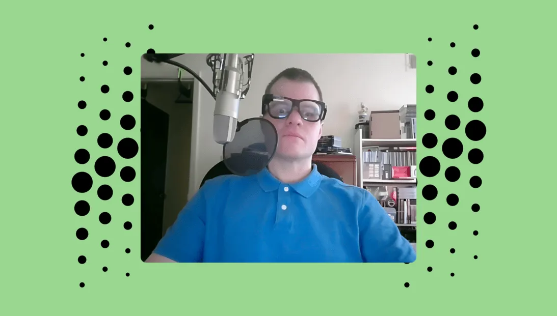 Stephen Clower, wearing Envision Glasses while seated in front of a professional microphone setup, with shelves of books and documents in the background.
