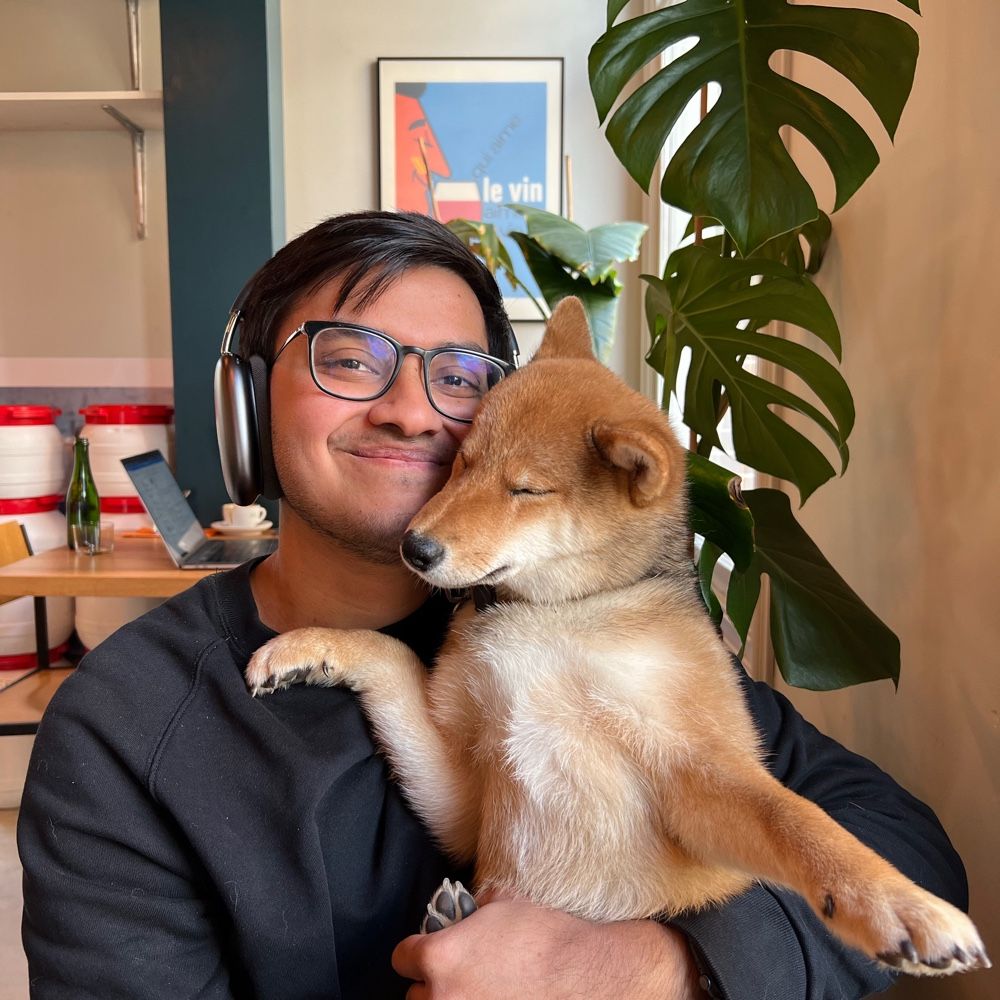 A photo of Amrith and his shiba inu dog named Sando in a cozy café in Amsterdam with a beautiful plant and random artwork in the background.